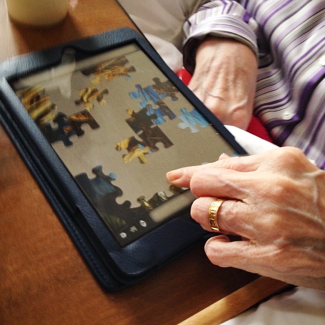 Mum sitting in her chair doing a jigsaw on the iPad – lovely to see